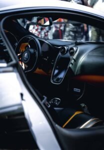 Luxury sports car interior with logo steering wheel, sleek dashboard, touchscreen, leather seats.
